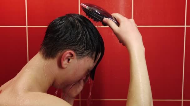 Ein junger Mann unter der Dusche. Ein Teenager wäscht sich im Badezimmer unter einem Strom aus warmem Wasser. - Filmmaterial, Video