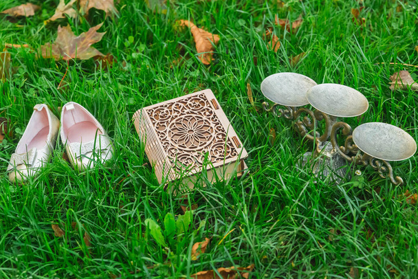 Małe rzeczy księżniczki: buty, trumna w postaci książki i antyczny świecznik w trawie - Zdjęcie, obraz