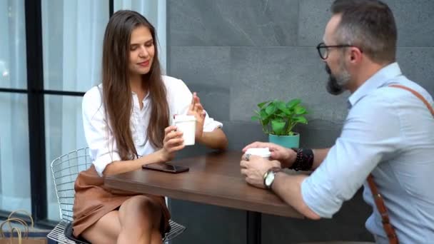 Νεαρός επιχειρηματίας και γυναίκα πίνουν καφέ. Αρσενικό και θηλυκό συζητούν τις εισερχόμενες πληροφορίες. - Πλάνα, βίντεο