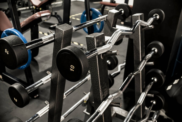 A rack of EZ and straight bar barbells with fixed weights at a gym or fitness club. - Fotó, kép