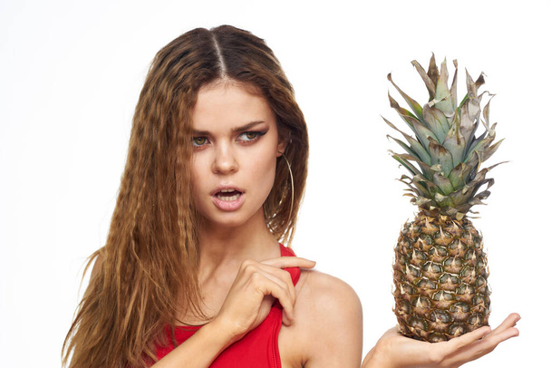 Femme avec ananas dans les mains cheveux ondulés rouge t-shirt fruits vacances d'été fond clair - Photo, image