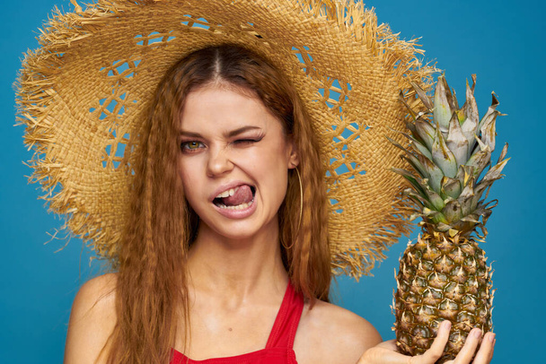 Nő egy szalmakalapban ananásszal a kezében hullámos haj egzotikus gyümölcsök nyár kék háttér nyaralás - Fotó, kép