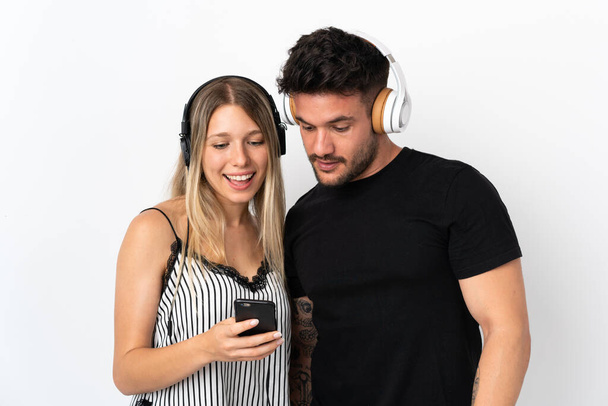 Young caucasian couple on white background listening music and looking to mobile - Foto, Bild