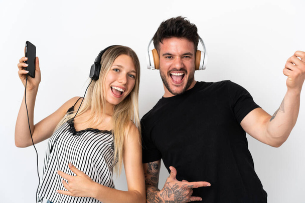 Young caucasian couple on white background listening music and doing guitar gesture - Foto, afbeelding