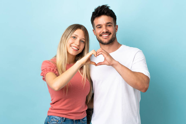 Young caucasian couple isolated on blue background making a heart with hands - Foto, Bild