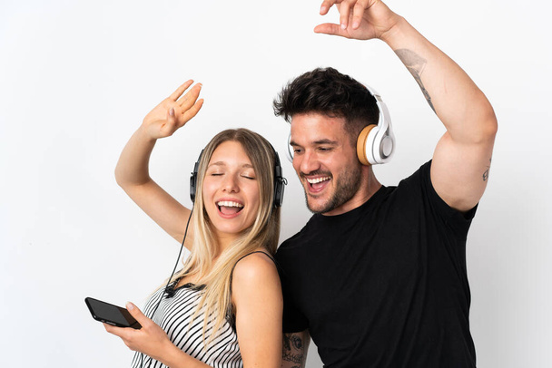 Young caucasian couple on white background listening music and dancing - Φωτογραφία, εικόνα