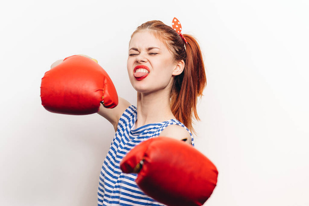 mujer pelirroja en guantes se dedica al boxeo sobre un fondo claro modelo de agresión - Foto, Imagen