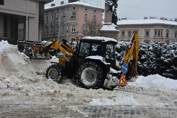 Lviv. Oekraïne. Februari 2021.Sneeuwruimer met draaiende borstel veegt sneeuw van voetpad op dijk in park. trekker met primeur en automatische borstel verwijdert sneeuw. Gemeentelijke dienst - Foto, afbeelding