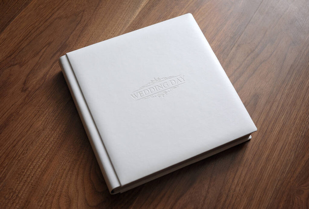 Album photo de mariage en cuir blanc avec couverture en relief repose sur une table en bois - Photo, image