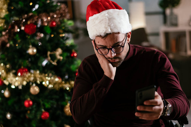 surullinen mies pyörätuolissa joulukuusi älypuhelimella - Valokuva, kuva