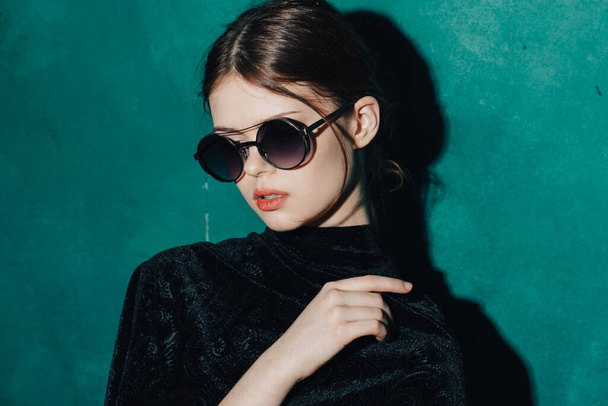 retrato de una joven con gafas de sol y un suéter negro fondo verde de cerca - Foto, Imagen