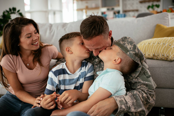 兵士と妻は子供と一緒に家で楽しんでいます。家族と一緒に床に座っている幸せな兵士. - 写真・画像