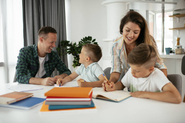 Родители помогают детям с домашним заданием. Маленькие мальчики учатся дома. - Фото, изображение
