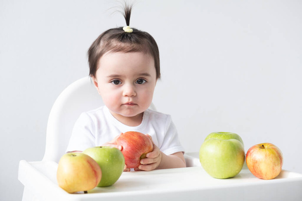 Bebek koltuğunda oturan bebek beyaz arka planda elma yiyor. Bebek önce katı yiyecekler - Fotoğraf, Görsel