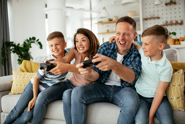 Padre y madre se divierten mientras juegan videojuegos con niños en casa. - Foto, imagen