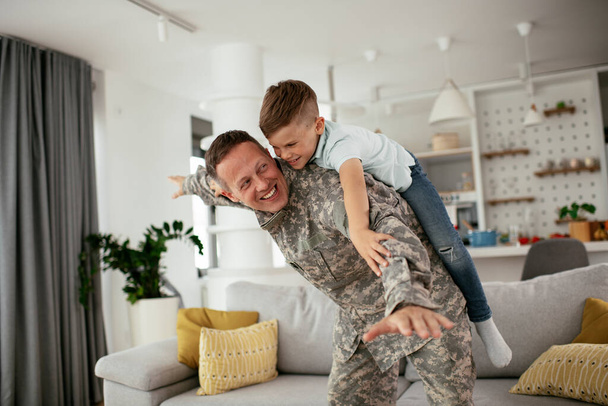 Soldato che si diverte con suo figlio a casa. Padre e figlio che giocano in salotto. - Foto, immagini