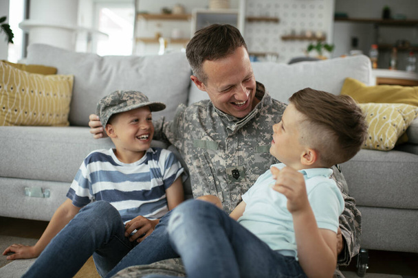 Щасливий солдат сидить на підлозі зі своєю сім'єю. Солдат насолоджується вдома з дітьми
. - Фото, зображення