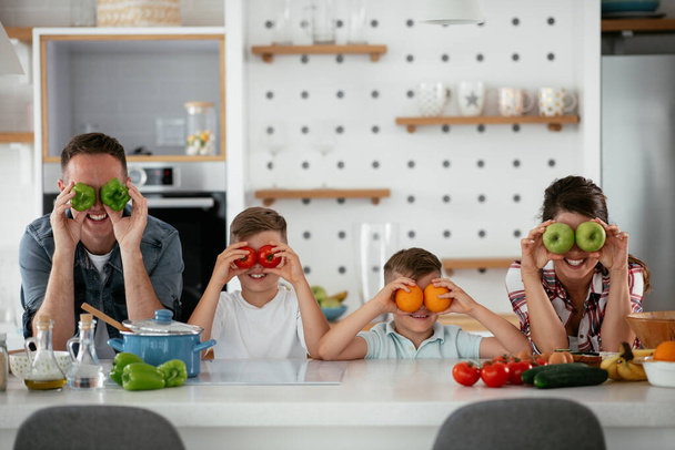 Mutter und Vater frühstücken mit ihren Söhnen. Junge Familie bereitet leckeres Essen in Küche zu und hat Spaß - Foto, Bild