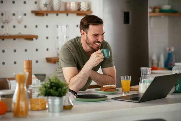 Young man having video call in the morning. Handsome man having breakfast in kitchen. - Foto, imagen