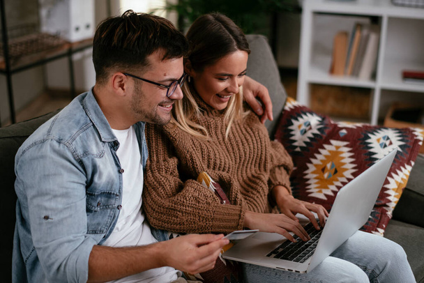 Young couple using credit card and laptop at home. Boyfriend and girlfriend buying online. - Photo, Image