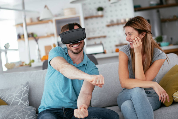 Couple heureux s'amuser avec des lunettes de réalité virtuelle dans le salon. Jeune couple jouant et appréciant les jeux vidéo avec casque VR à la maison. - Photo, image