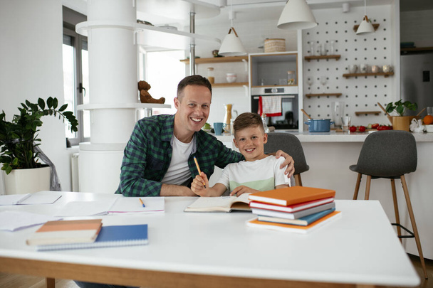 Vader helpt zijn zoon met huiswerk thuis. Kleine jongen leren thuis. - Foto, afbeelding