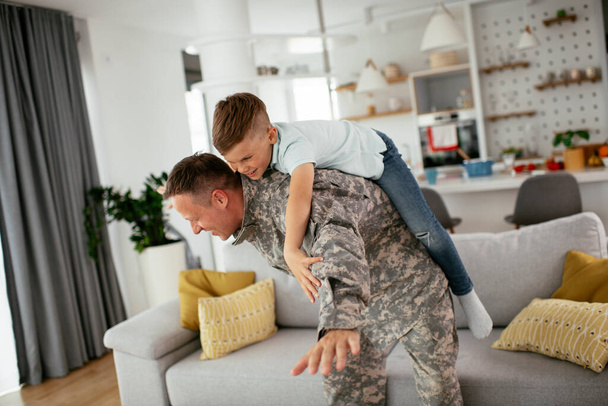 Soldier having fun with his son at home. Father and son playing in living room. - Zdjęcie, obraz