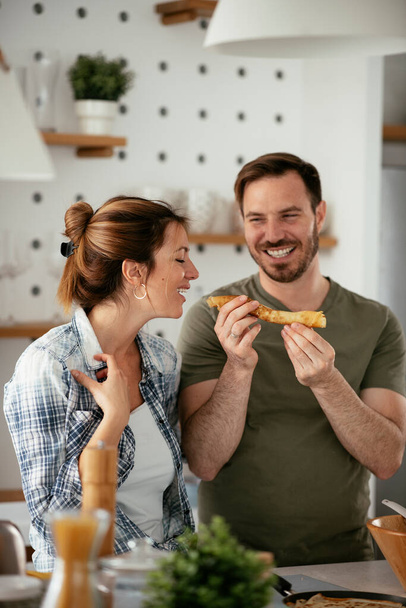 Jeune couple faisant des crêpes à la maison. Couple aimant s'amuser en cuisinant. - Photo, image