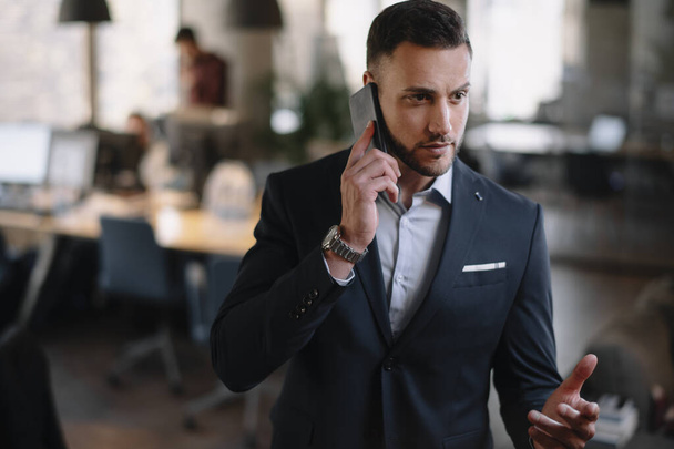 Uomo d'affari in giacca e cravatta con smartphone moderno in ufficio. - Foto, immagini