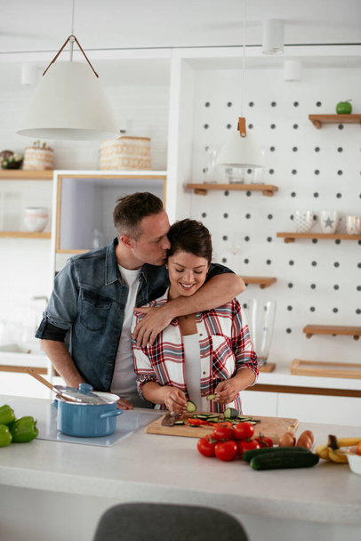 若い夫婦が家で朝食を作っている。キッチンでサンドイッチを食べるカップルを愛し. - 写真・画像