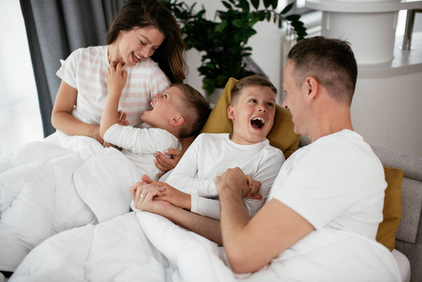 Young family enjoying in bed. Happy parents with sons relaxing in bed. - Foto, Imagen