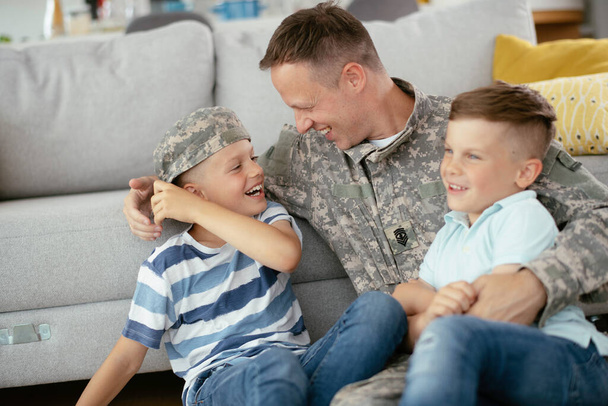 Padre in uniforme trascorrere del tempo insieme ai figli a casa vicino al divano  - Foto, immagini