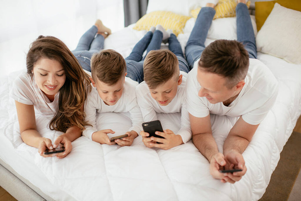 Perhe käyttää matkapuhelimia. Vanhemmat ja lapset käyttävät älypuhelimia kotona. - Valokuva, kuva