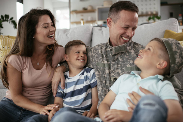Soldat und seine Frau genießen zu Hause mit Kindern. Glücklicher Soldat sitzt mit seiner Familie auf dem Boden. - Foto, Bild