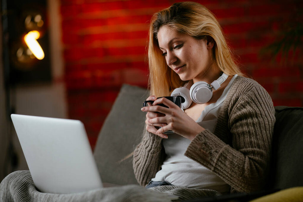 Belle femme blonde regardant un film sur son ordinateur portable à la maison. - Photo, image