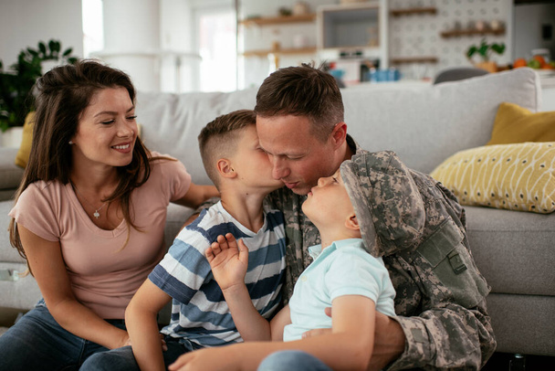兵士と妻は子供と一緒に家で楽しんでいます。家族と一緒に床に座っている幸せな兵士. - 写真・画像
