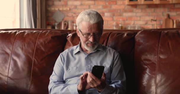 Happy middle aged 60s old man in glasses using smartphone. - Video, Çekim