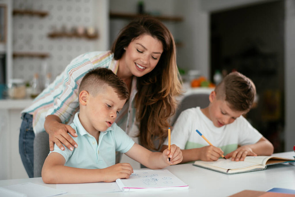 joven madre haciendo la tarea con sus hijos en casa - Foto, imagen