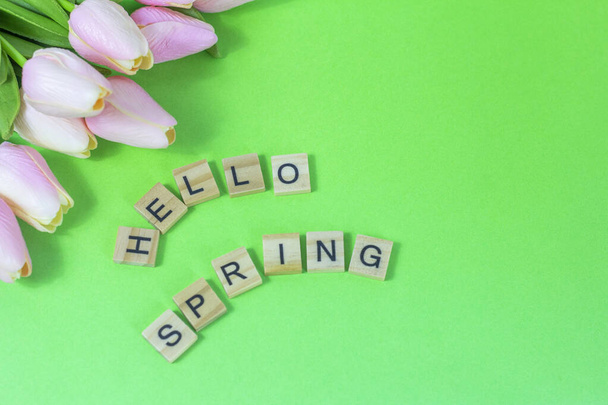 Hello spring.Wooden blocks with an inscription and tulips on a green background.The concept of the beginning of the long-awaited spring. - Photo, Image