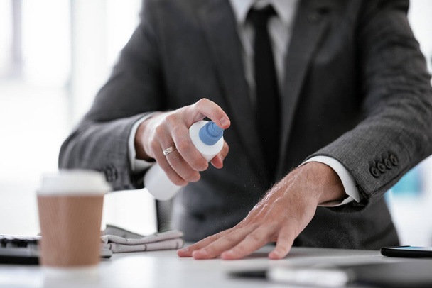 Επιχειρηματίας με κοστούμι απολυμαίνει τα χέρια του στο γραφείο. - Φωτογραφία, εικόνα