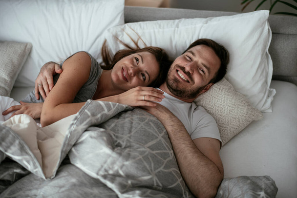 Young loving couple in bed. Top view of happy couple relaxing in bed. - 写真・画像