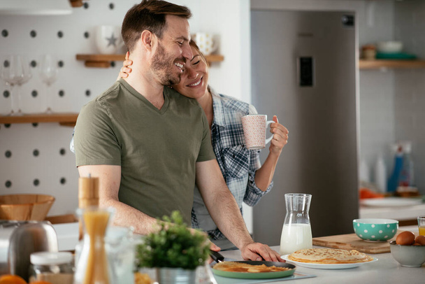 Νεαρό ζευγάρι φτιάχνει τηγανίτες στο σπίτι. Αγαπημένο ζευγάρι που διασκεδάζει ενώ μαγειρεύει. - Φωτογραφία, εικόνα