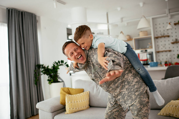 Soldado se divertindo com seu filho em casa. Pai e filho brincando na sala de estar. - Foto, Imagem