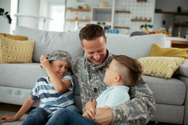 Boldog katona ül a földön a családjával. Katona élvezi otthon a gyerekekkel. - Fotó, kép