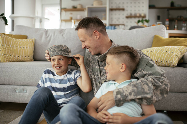 Feliz soldado sentado en el suelo con su familia. Soldado disfrutando en casa con niños. - Foto, imagen