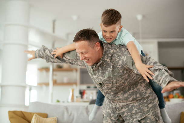 Żołnierz bawiący się z synem w domu. Ojciec i syn bawią się w salonie. - Zdjęcie, obraz