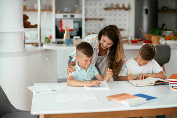 junge Mutter macht Hausaufgaben mit ihren Söhnen zu Hause - Foto, Bild