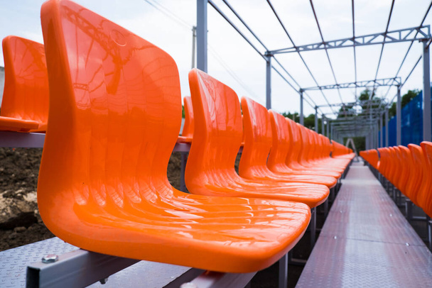 Leere Tribünen mit Plastiksitzen, Stühle für Fans im örtlichen Sportstadion - Foto, Bild