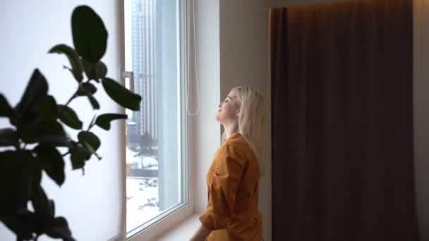 Young woman opening curtain looking through window. Happy confident lady enjoying beautiful view and dreaming at home. Smiling girl contemplating feeling hope peaceful morning standing in apartment - Footage, Video