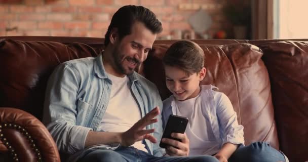 Young father showing educational application on cellphone to small son. - Materiał filmowy, wideo